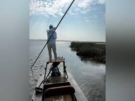A person stands on the bow of a boat, using a pole to navigate through shallow waters, showcasing an adventurous day of fishing or exploring the wetlands.