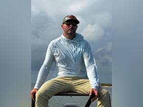 A man sits confidently on a boat, showcasing a relaxed vibe against a backdrop of cloudy skies and water — perfect for fishing or leisure outings.