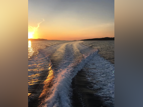 A stunning sunset over tranquil waters, showcasing the beautiful wake of a boat as it glides through the sea — perfect for capturing the essence of a serene evening on the water.