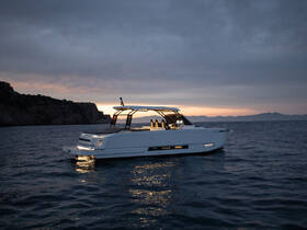 A sleek yacht glides through calm waters at dusk, showcasing its modern design against a stunning coastal backdrop.