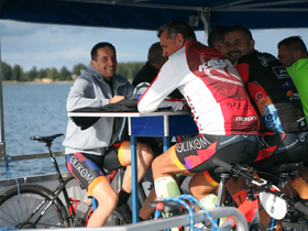 A group of cyclists enjoys a moment of camaraderie at a table on a boat, overlooking the water — perfect for post-ride relaxation and socializing.