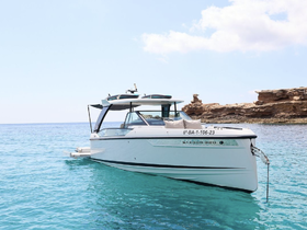 A sleek Saxdor 320 yacht glides through crystal-clear waters, showcasing its elegant design against a stunning coastal backdrop.