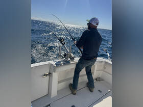 A fisherman reels in a catch aboard a boat, showcasing the thrill of deep-sea fishing on a sunny day.