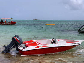 A vibrant red speedboat with a Yamaha engine is docked on the shore, showcasing its sleek design against the clear turquoise waters.