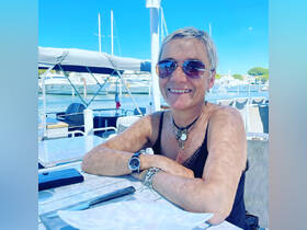 A woman enjoys a sunny day dining on a boat, smiling with a beautiful marina backdrop — perfect for leisurely meals on the water.