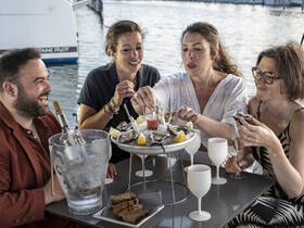 A lively group enjoys a seafood feast with oysters and cocktails on a boat, perfect for celebrating special moments on the water.