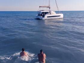 Two friends enjoy a refreshing swim in the ocean while a catamaran sails nearby, capturing the essence of fun and adventure on the water.