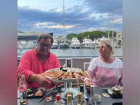 A couple enjoys a seafood feast at a marina restaurant, surrounded by yachts and a picturesque sky — perfect for a memorable dining experience by the water.