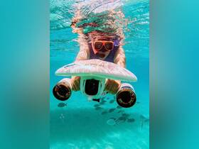 An adventurous snorkeler explores the underwater world while using a submersible device, surrounded by vibrant fish in crystal-clear waters.