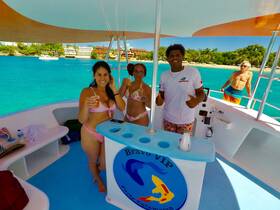 A lively group enjoys drinks aboard a catamaran, celebrating under the sun with stunning turquoise waters in the background — perfect for a fun day on the water.