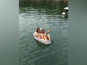 Two friends enjoy a sunny day on the water, relaxing on an inflatable float while sipping drinks — a perfect summer getaway moment.