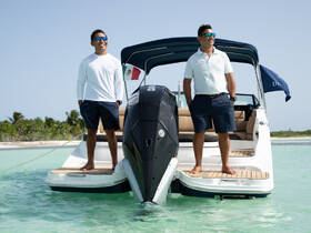 Two crew members stand proudly on the bow of a boat, showcasing their smiles against a beautiful ocean backdrop — perfect for highlighting the friendly service on your next boating adventure.