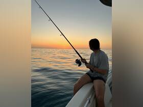 A young man enjoys fishing at sunset, capturing the serene beauty of the ocean while engaging in a popular on-water activity.