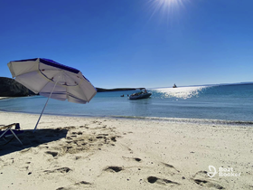 A serene beach scene featuring a boat on the water and an umbrella on the shore, perfect for a relaxing day under the sun.