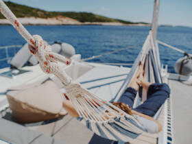 A guest relaxes in a hammock aboard a catamaran, enjoying the serene ocean views on a sunny day — perfect for unwinding during a sailing adventure.