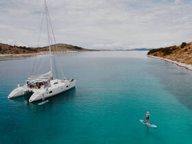 A serene scene featuring a paddleboarder gliding through turquoise waters near a catamaran, showcasing the beauty of water activities and stunning landscapes.