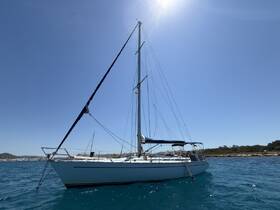 A beautiful sailboat glides through clear waters, showcasing its elegant design against a backdrop of a sunny sky and distant coastline.