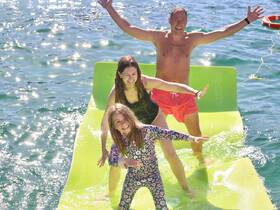 A joyful family enjoys a fun day on a floating mat in the water, showcasing laughter and togetherness during their boating adventure.