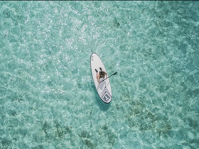Aerial view of a person paddleboarding in crystal-clear waters, showcasing the beauty of on-water activities in tropical destinations.