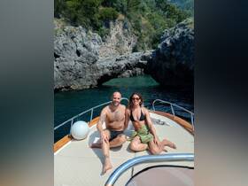 A couple enjoys a sun-soaked moment on the deck of a boat, surrounded by stunning rocky cliffs and clear waters — perfect for a romantic getaway.