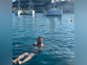A man enjoys a relaxing swim in crystal-clear waters, surrounded by sailboats — a perfect scene for summer adventures and water activities.