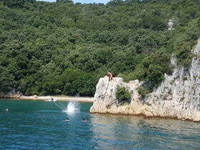 A thrilling scene of cliff diving and swimming in clear waters, showcasing a group enjoying a summer adventure in a picturesque setting.