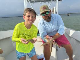 A child and an adult proudly display a starfish and a stingray aboard a boat, showcasing a memorable wildlife encounter during their aquatic adventure.