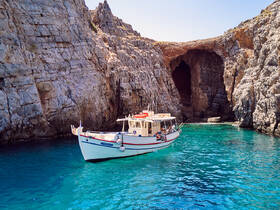 A charming fishing boat navigates through crystal-clear waters near stunning rocky cliffs, perfect for exploring hidden coves and enjoying a day on the water.