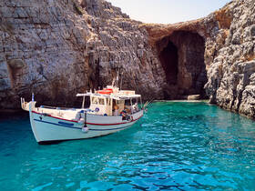 A charming fishing boat is docked in crystal-clear turquoise waters, surrounded by stunning rocky cliffs — a perfect spot for fishing tours and exploring hidden caves.