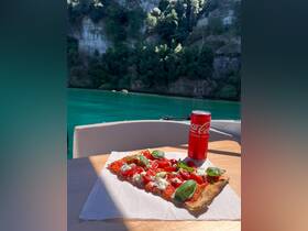 A delicious pizza and a refreshing Coca-Cola are beautifully presented on a table aboard a boat, perfect for enjoying a meal while taking in the stunning turquoise waters.