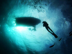 A captivating underwater scene featuring divers exploring the ocean depths, with a silhouette of a boat above and schools of fish swimming nearby.