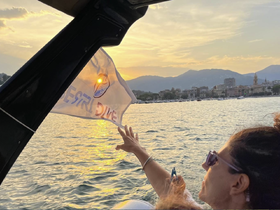 A woman joyfully waves a flag while enjoying a sunset view from a boat, capturing the essence of a perfect evening on the water.