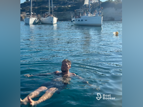 A man enjoys a relaxing swim in crystal-clear waters, surrounded by boats in the background — a perfect scene for summer adventures on the water.