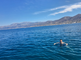 A person enjoys a refreshing swim in the clear blue ocean, with stunning mountain scenery in the background — a perfect moment for adventure seekers.