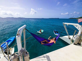 A vibrant scene of relaxation on the water, featuring a woman lounging in a hammock while another person enjoys kayaking nearby — perfect for a fun day on the Caribbean sea.