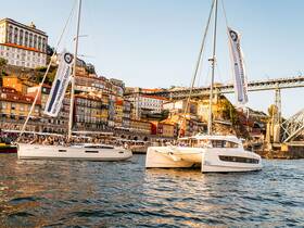 Two sailing boats filled with guests enjoy a scenic tour along the picturesque waterfront of Porto, showcasing vibrant buildings and the iconic bridge.