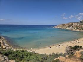 A picturesque beach scene with sunbathers and swimmers enjoying the clear turquoise waters, perfect for a relaxing day by the coast.