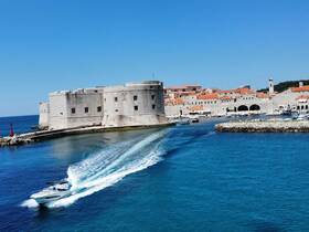 A speedboat glides through the vibrant waters of a picturesque harbor, showcasing stunning coastal architecture and a clear blue sky — a perfect scene for boating enthusiasts and travelers.