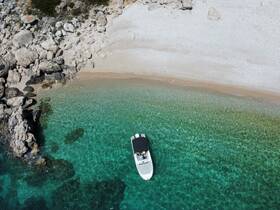 Aerial view of a sleek boat anchored in crystal-clear turquoise waters, surrounded by rocky shores — a perfect spot for relaxation and exploration.