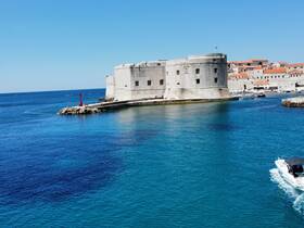 A stunning view of a historic fortress by the coastline, with a boat cruising in the clear blue waters — a perfect representation of the beautiful scenery found in coastal destinations.