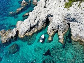 Aerial view of a boat navigating through crystal-clear turquoise waters, surrounded by rocky formations — an ideal scene for exploring coastal landscapes.