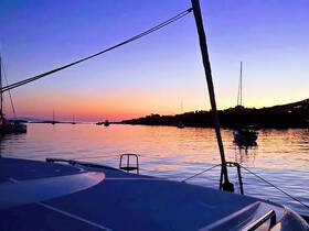 A serene sunset view from the deck of a catamaran, showcasing calm waters and distant boats, perfect for tranquil evening cruises.