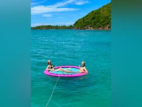 Two friends enjoy a refreshing day on a floating mat in crystal-clear waters, sipping cocktails and soaking up the sun — a perfect way to celebrate summer adventures.