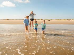 A joyful family moment as children splash in the shallow waters of the beach, capturing the essence of fun and togetherness during a sunny day by the sea.