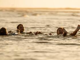 Three children enjoy a playful swim in the warm waters at sunset, capturing the joy of summer water activities.