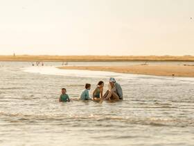 A joyful family enjoys a playful moment in shallow waters, creating lasting memories at the beach during sunset.