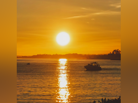 A serene sunset view over the water with a boat cruising in the foreground, creating a picturesque scene perfect for evening outings.