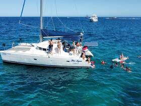 A lively group enjoys a day on the water, swimming and playing around a catamaran, making it a perfect outing for families and friends.