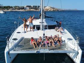 A lively group enjoys a sunny day on a catamaran, celebrating and sunbathing on the deck — perfect for a fun day out on the water.