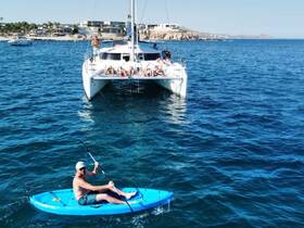 A man enjoys kayaking in the vibrant waters while a group relaxes on a catamaran in the background, showcasing the perfect blend of adventure and leisure on the water.